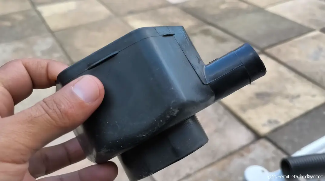 Rainwater diverter connected to a downpipe and feeding a garden rain barrel